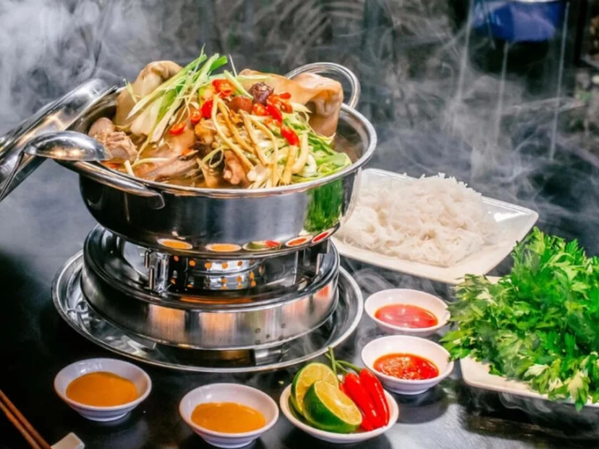 Nồi lẩu dê nghi ngút khói bày biện hấp dẫn cùng rau, bún và nước chấm.