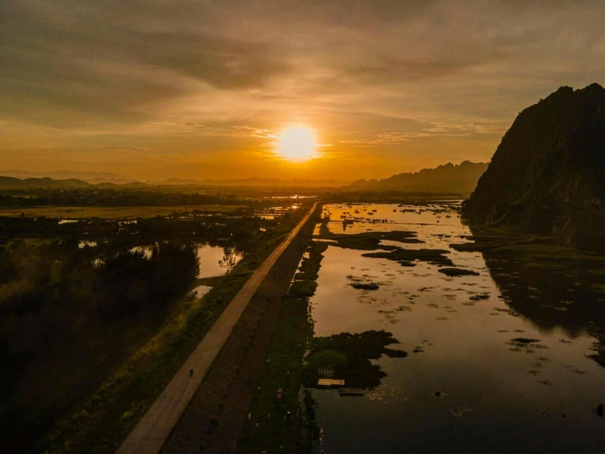 Hoàng hôn nhuộm vàng con đường dài giữa đầm nước và núi đá tại Ninh Bình.