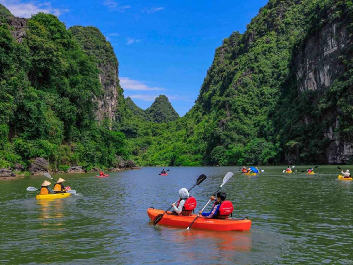 Du khách chèo kayak trên sông xanh giữa núi đá vôi hùng vĩ.