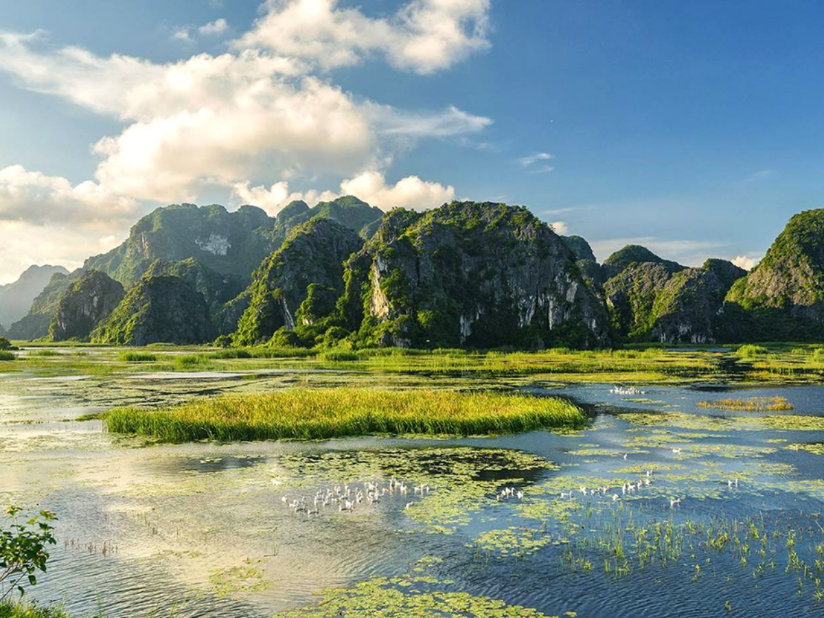 Đầm nước trải rộng dưới núi đá vôi xanh tạo cảnh quan yên bình.